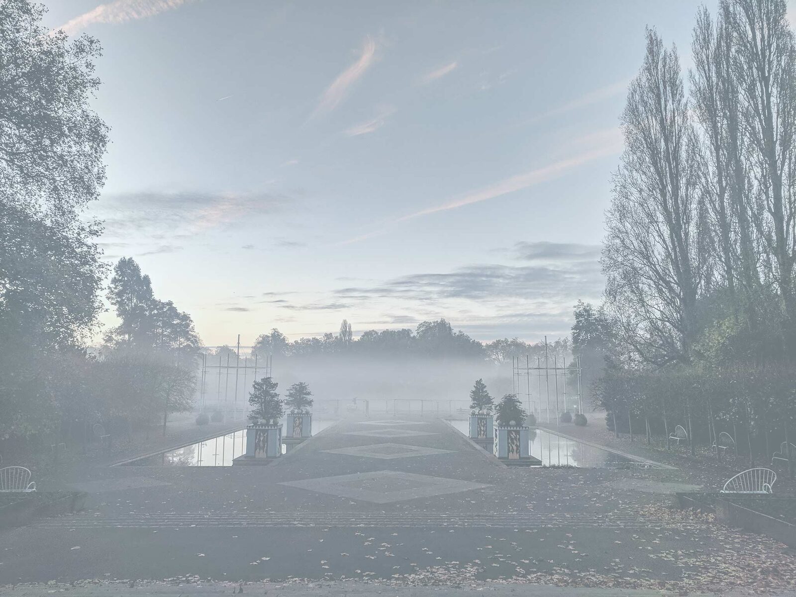A misty autumn morning over an ornamental lake lined with tall trees